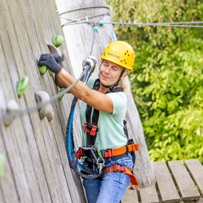 Junger Mann mit Sicherung  und Helm steht auf einer Plattform im Kletterpark
